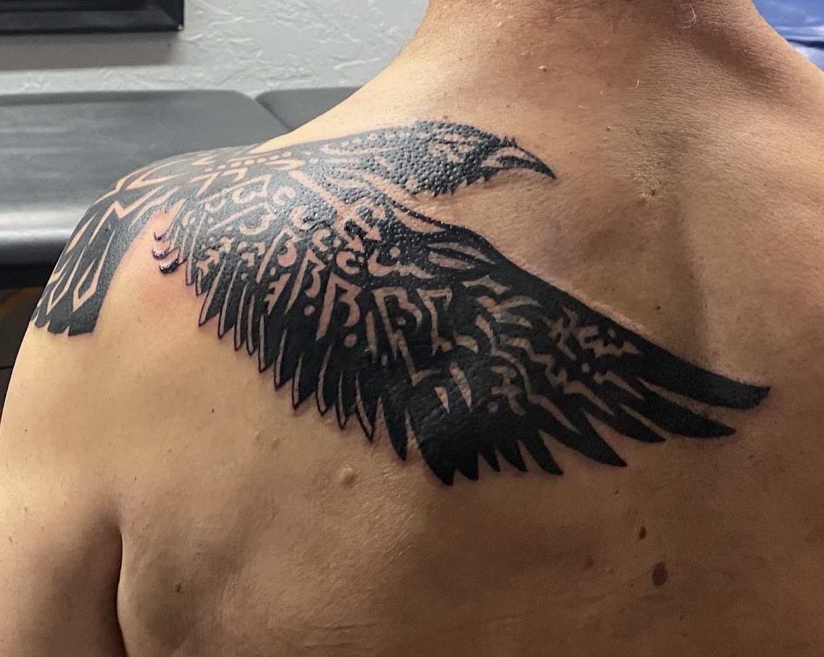 Blackwork raven wing tattoo on the shoulder